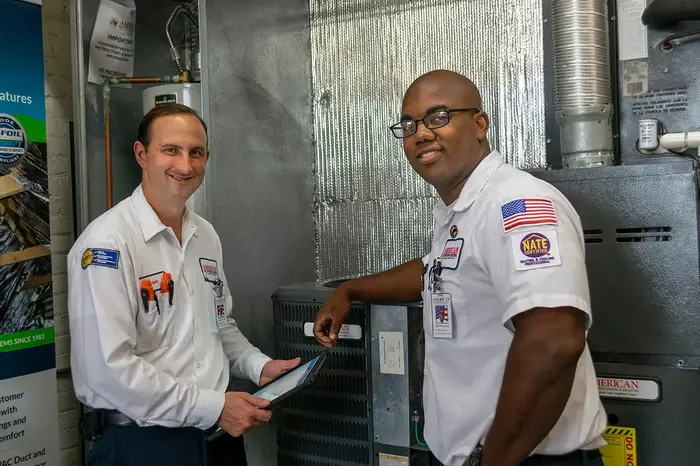 HVAC technicians smiling in front of an air conditioner